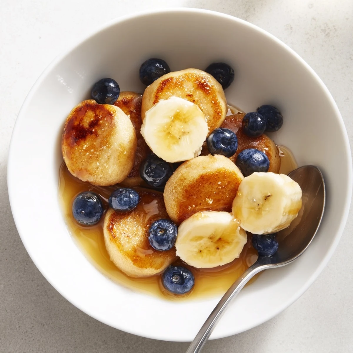 Tiny, fluffy pancakes resembling cereal, drizzled with syrup and topped with bananas.  
