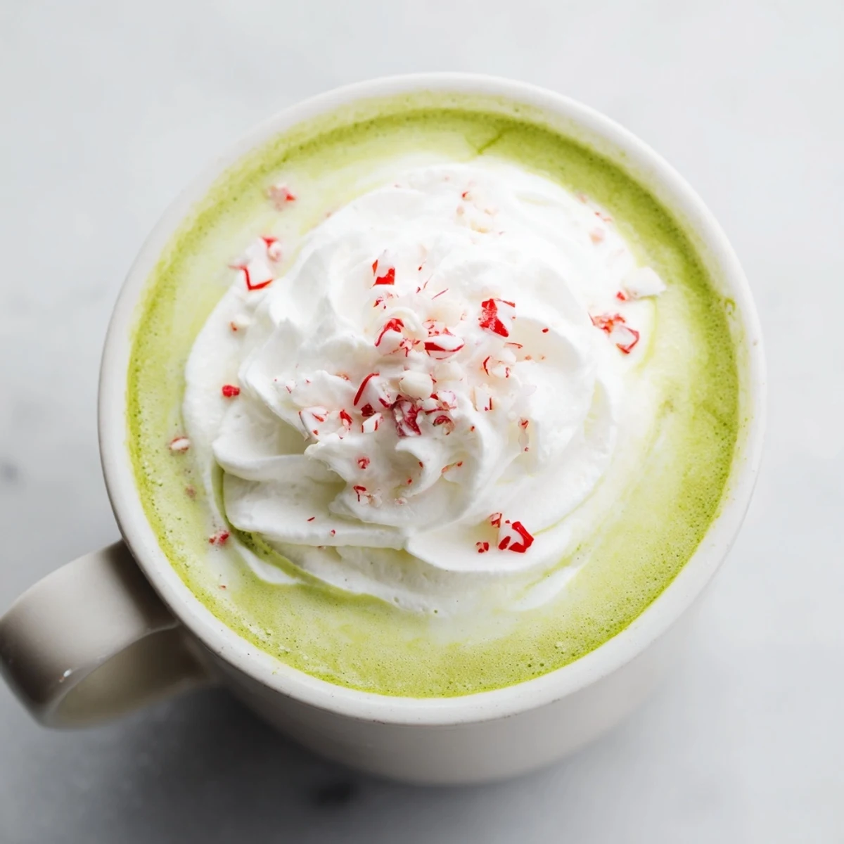 A warm, creamy Cozy Peppermint Matcha Christmas Latte topped with delightful whipped cream and candies.