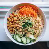 A fresh Peanut Chickpea Rice Bowl featuring tender chickpeas, crisp carrots, cabbage, and cucumber with a drizzle of zesty peanut dressing.