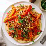 A hearty vegetarian main dish featuring caramelized vegetables, toasted seeds, and fresh parsley on a smooth, savory hummus base.  