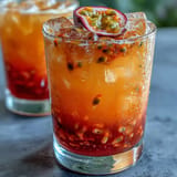 A colorful non-alcoholic beverage featuring passionfruit, orange, and pineapple juices, beautifully layered to resemble a sunrise and garnished with fresh mint and orange slices.