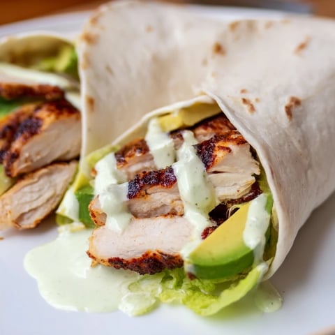 A close-up of a Smoky Chipotle Chicken Wrap sliced in half, revealing layers of tender chicken, creamy avocado, crisp lettuce, and drizzled Greek yogurt sauce.