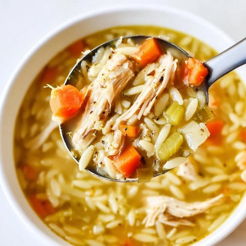 Steaming bowl of Lemon Pepper Chicken Orzo Soup, featuring tender shredded chicken, bright lemon zest, and fresh parsley garnish.