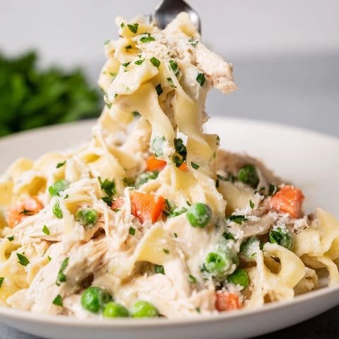 Steaming Spring Chicken Noodle Skillet features tender shredded chicken, carrots, and peas coated in a creamy, comforting sauce.