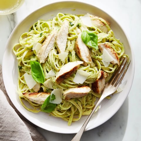 Creamy avocado chicken pasta served in a white bowl, topped with fresh basil and grated Parmesan.