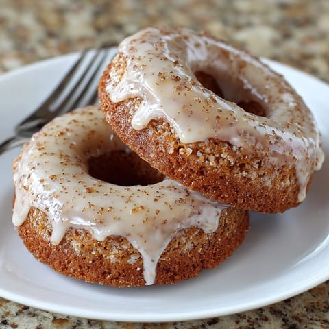 Warm, freshly-baked spiced apple cider donuts, glistening with sweet glaze, perfect for autumn.