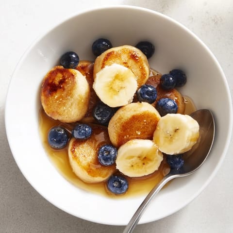 Tiny, fluffy pancakes resembling cereal, drizzled with syrup and topped with bananas.  