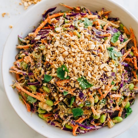 A generous bowl of Crunchy Thai Peanut Salad topped with chopped peanuts and fresh cilantro, served with lime wedges.