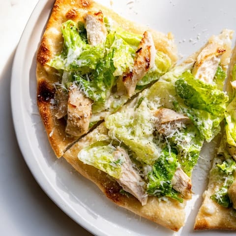 Slice of chicken Caesar flatbread topped with juicy grilled chicken and crisp lettuce on a rustic board.  