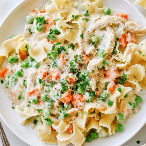 A close-up of Spring Chicken Noodle Skillet reveals golden egg noodles, vibrant vegetables, and fresh parsley garnish in a rustic skillet.