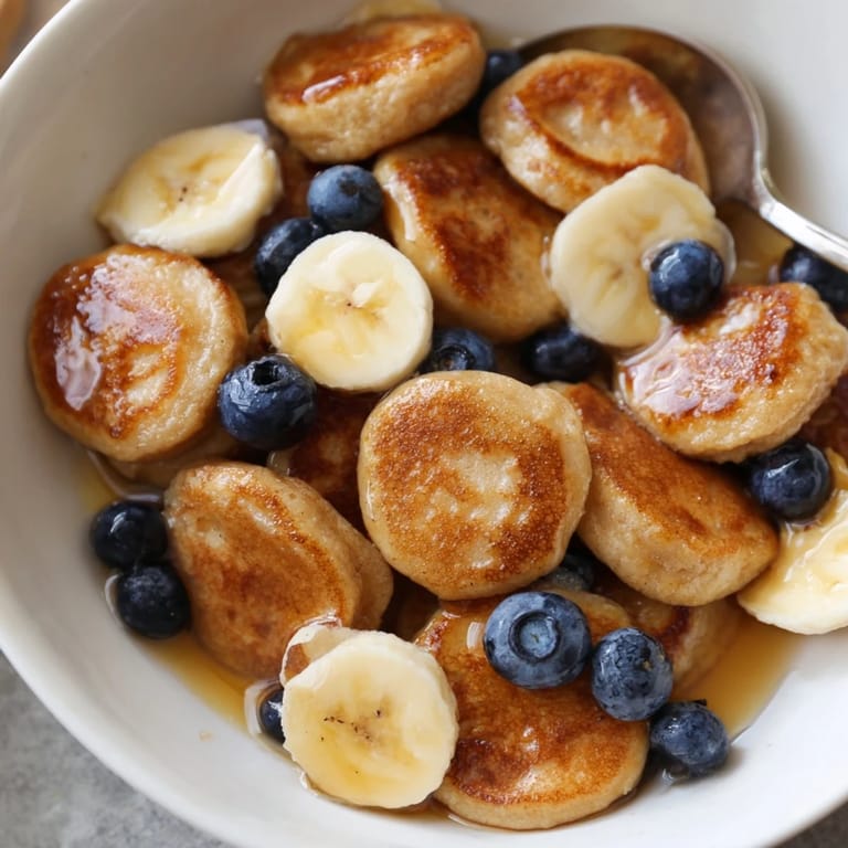 Golden, crispy mini pancake cereal served warm in a bowl with honey drizzles.
